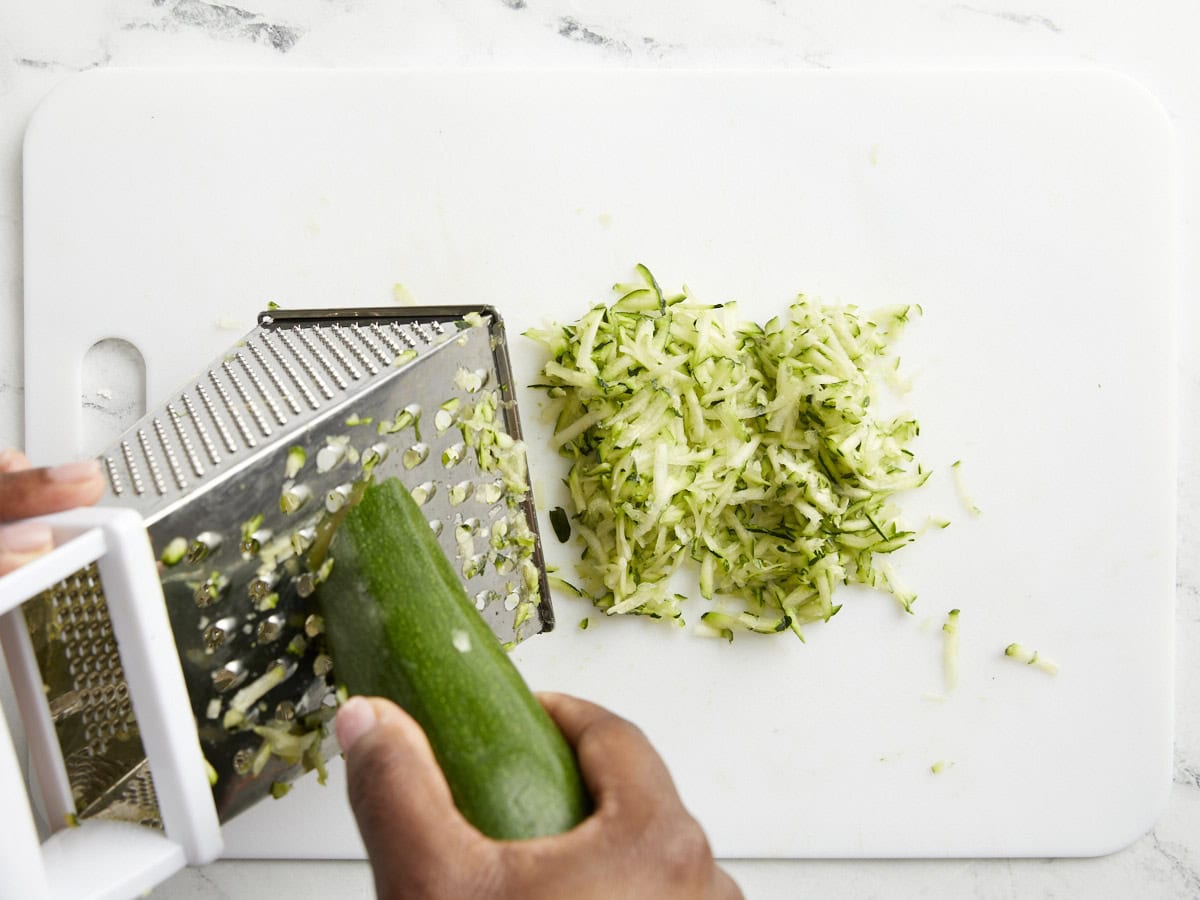 Zucchini being grated on a box grater.