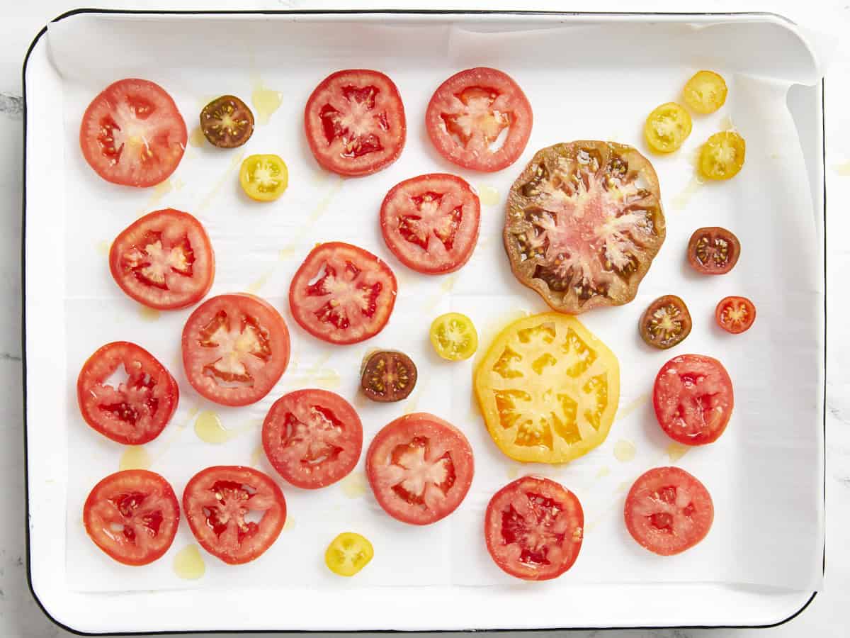 Sliced tomatoes on a baking sheet drizzled with olive oil.