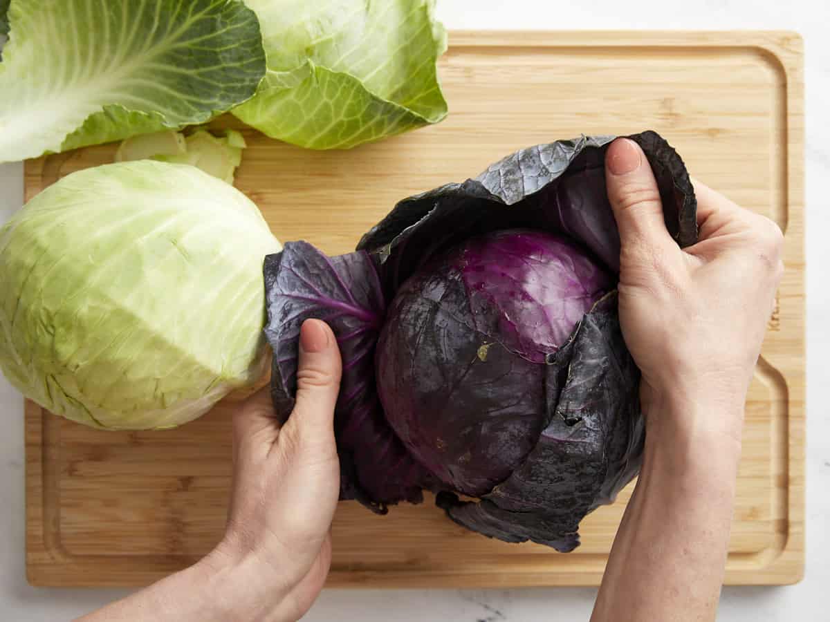 A hand peeling the outer leaves off a red cabbage.