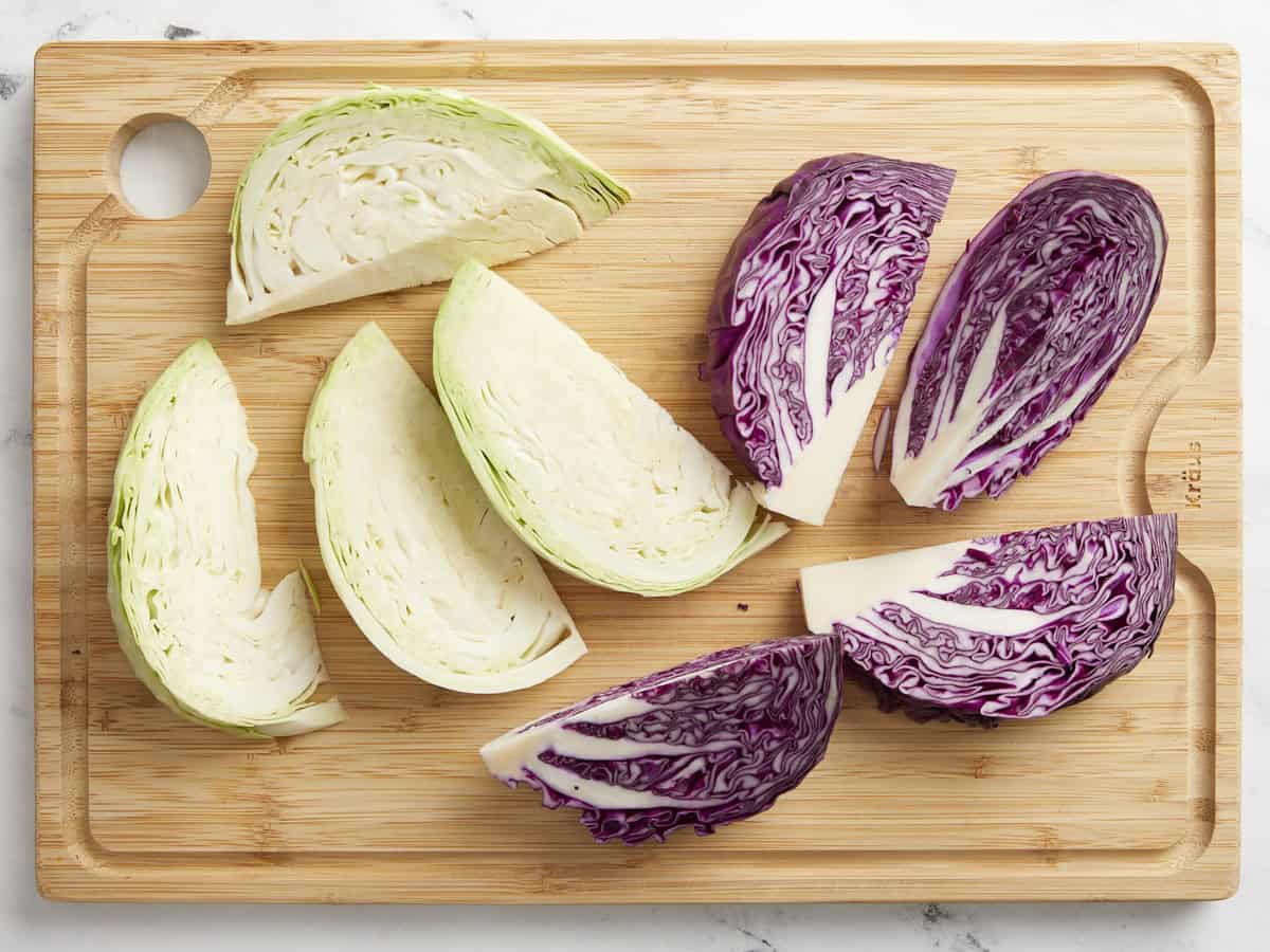 Green and red cabbage wedges on a chopping board.
