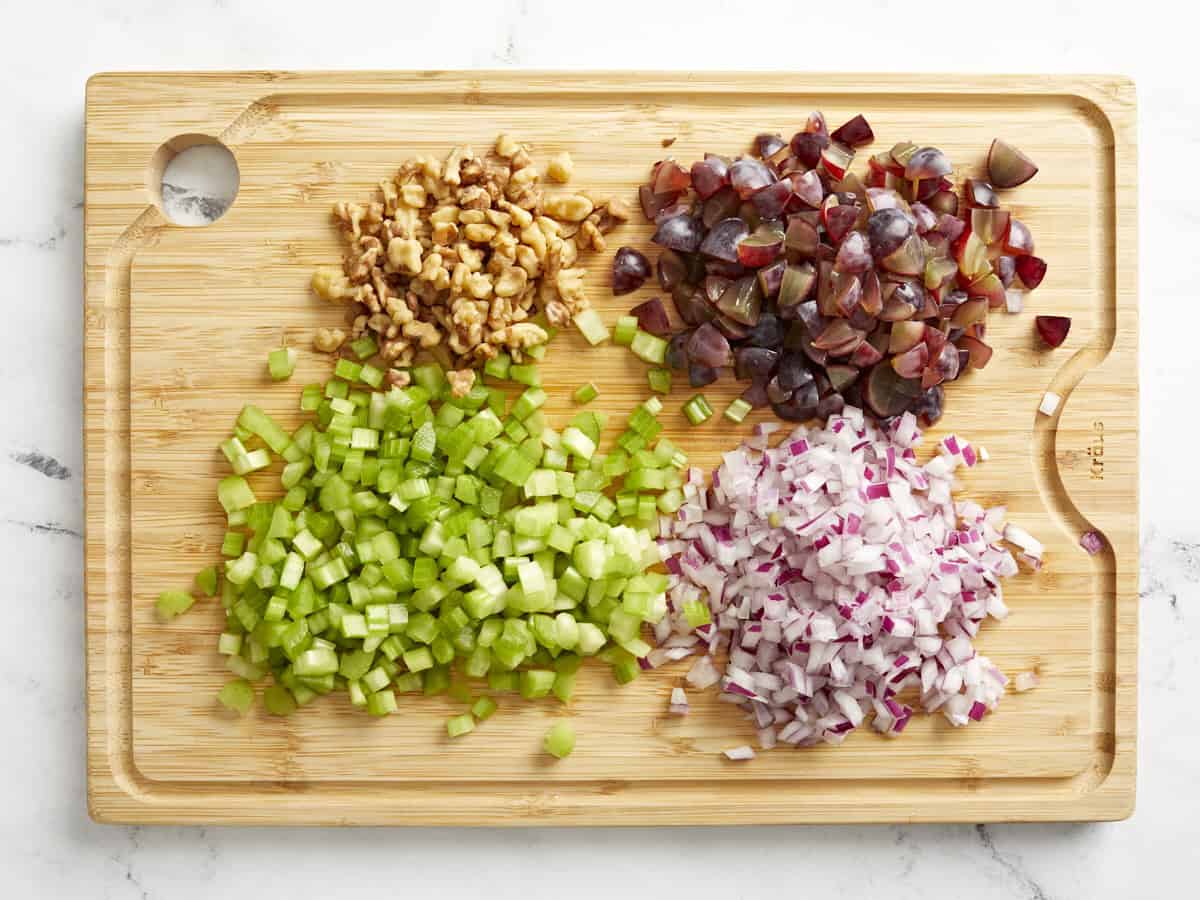 Diced ingredients for chicken salad on a wooden chopping board.