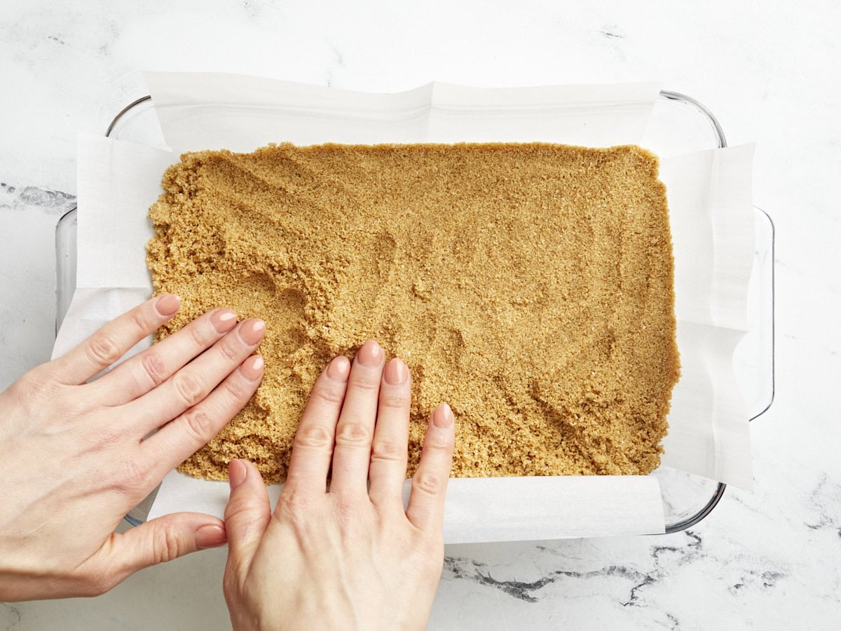 Hands pressing down the crust for key lime pie bars into a baking dish.