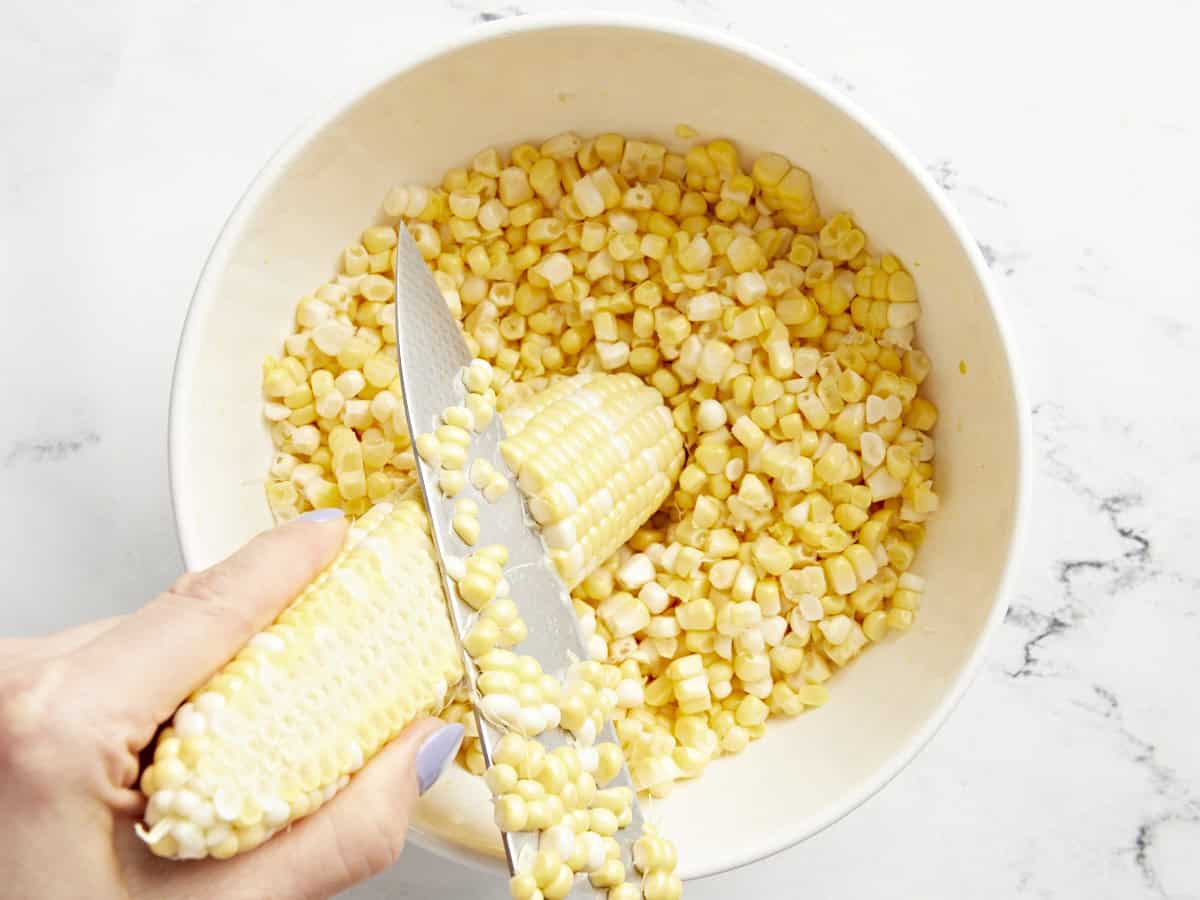 A knife shaving corn kernels off a corn cob.