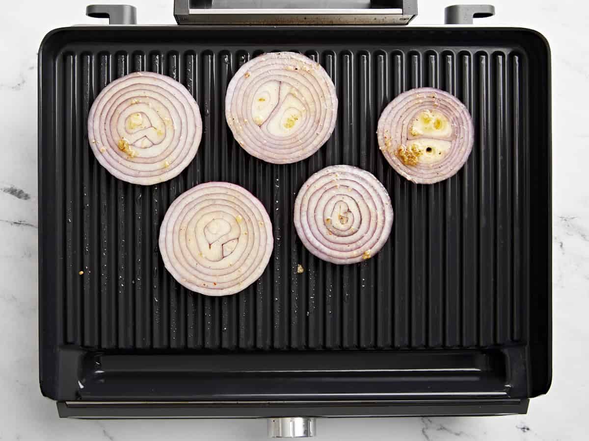 Overhead view of sliced red onions on a grill.
