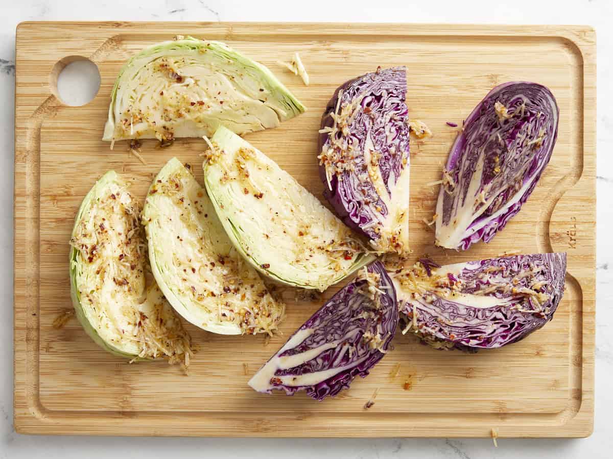 Green and red cabbage wedges topped with a Parmesan cheese mixture on a wooden chopping board.