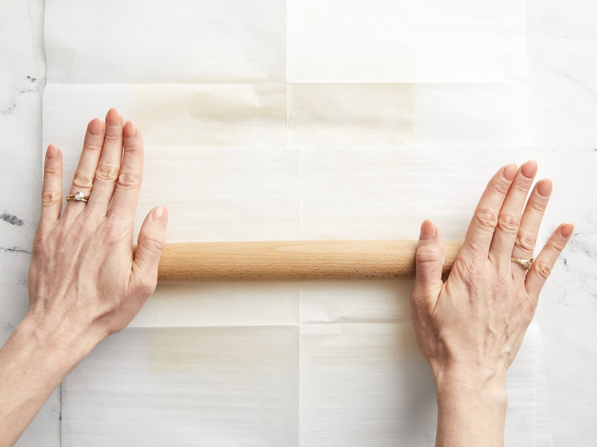 Hands rolling out a sheet of puff pastry dough.