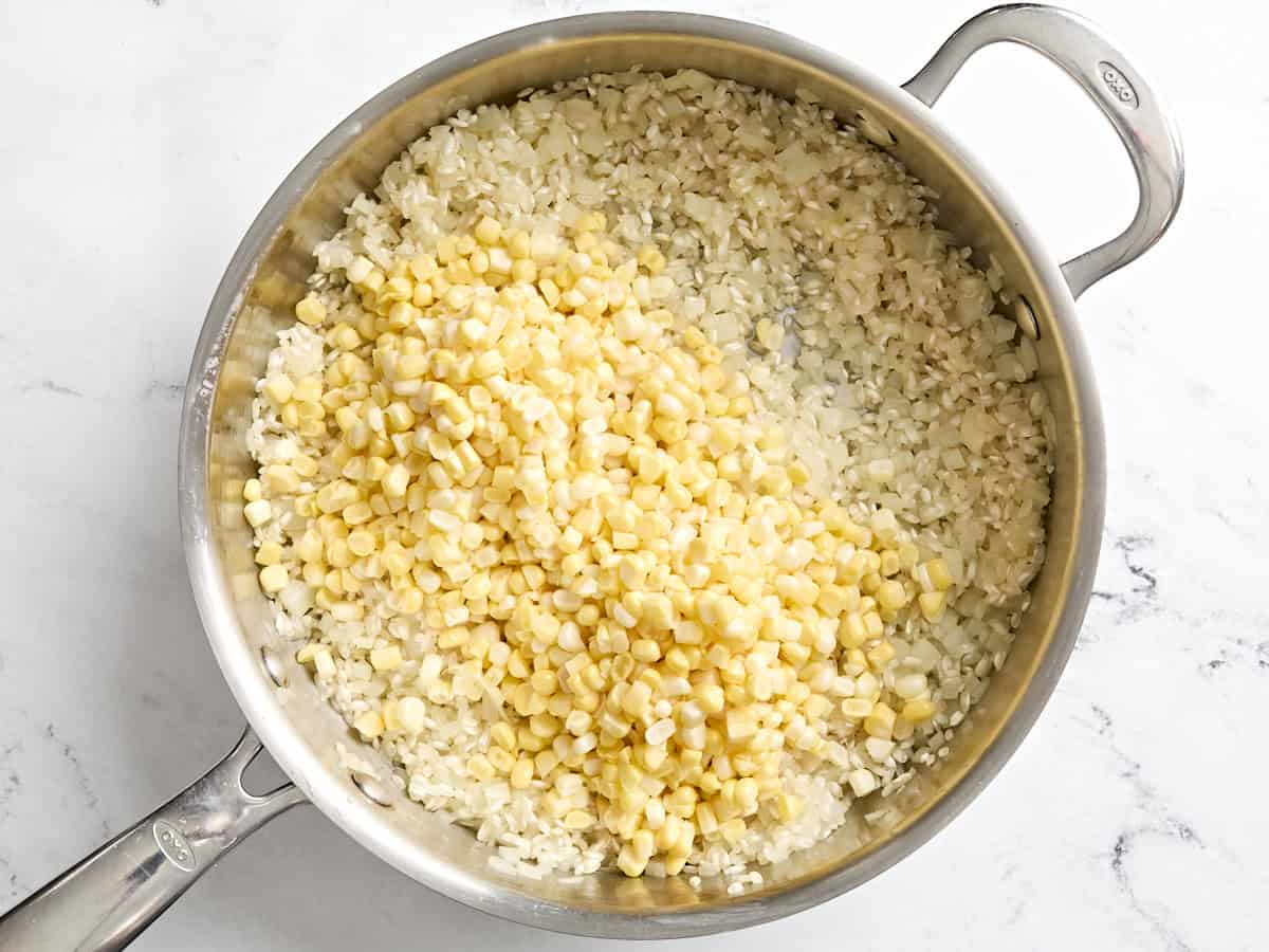 Corn kernels added to arborio rice to make sweet corn risotto in a skillet.
