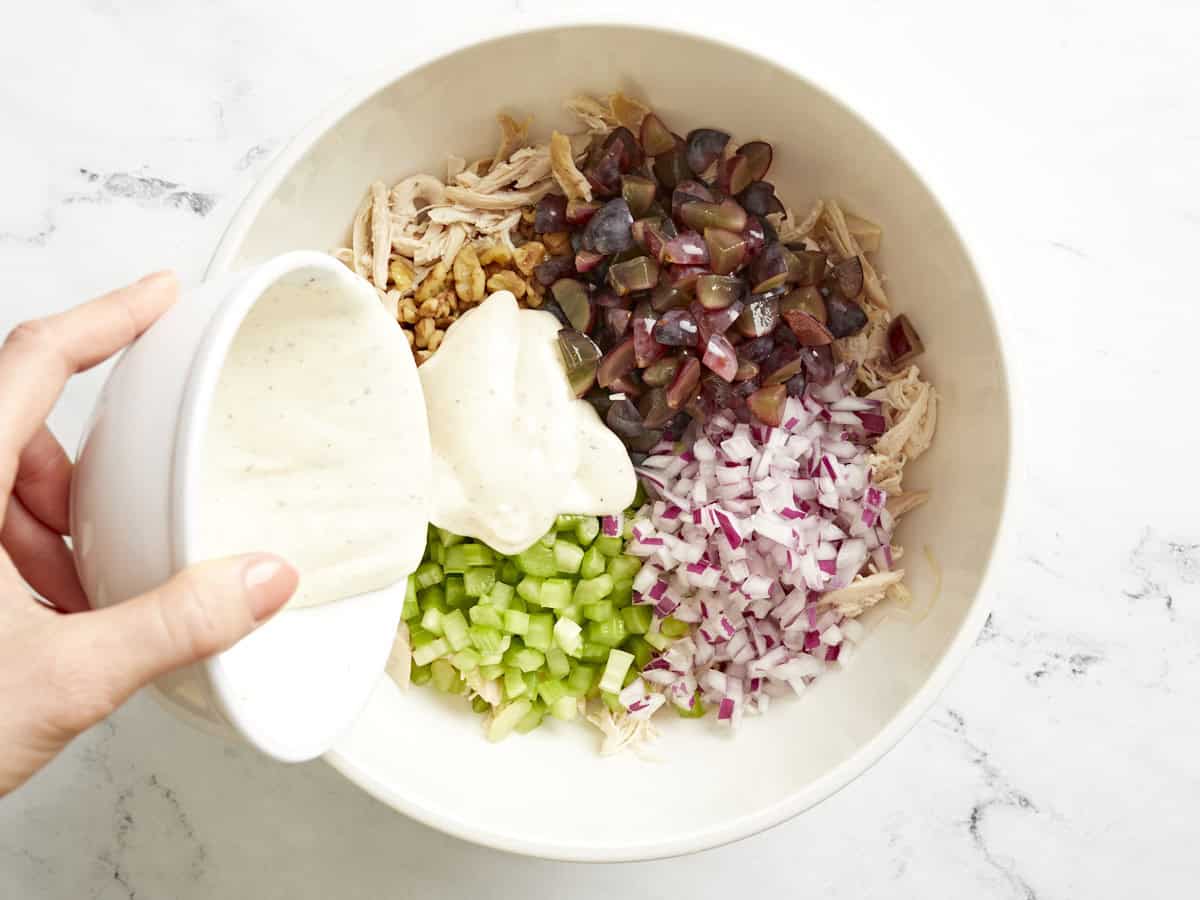 Dressing being poured onto the ingredients for chicken salad in a bowl.