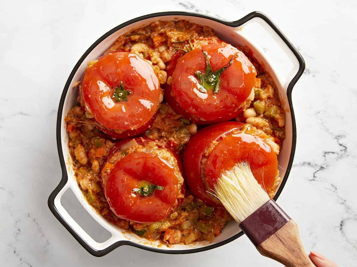 Tuscan white bean stuffed tomatoes in a baking dish being brushed with oil.