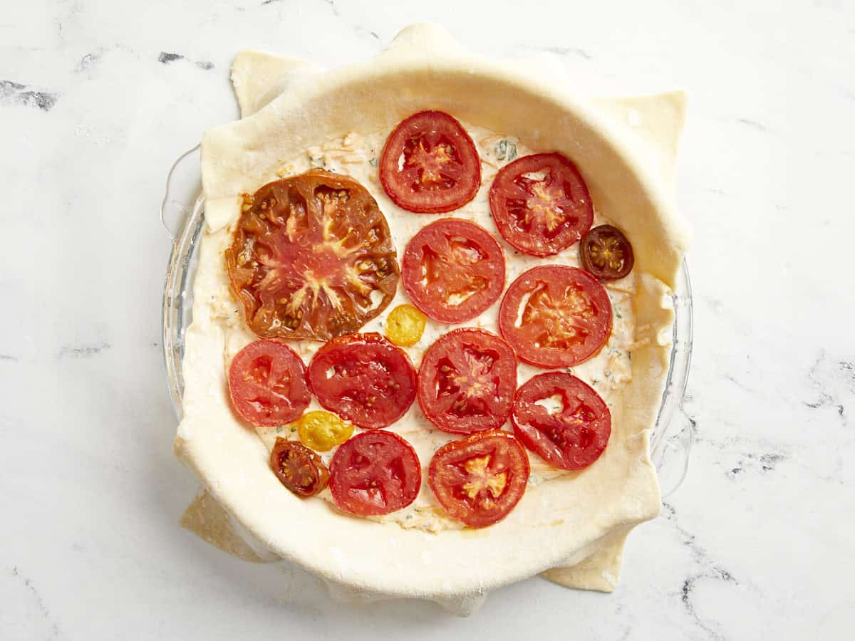 Puff pastry sheet in a glass pie pan filled with tomato pie filling