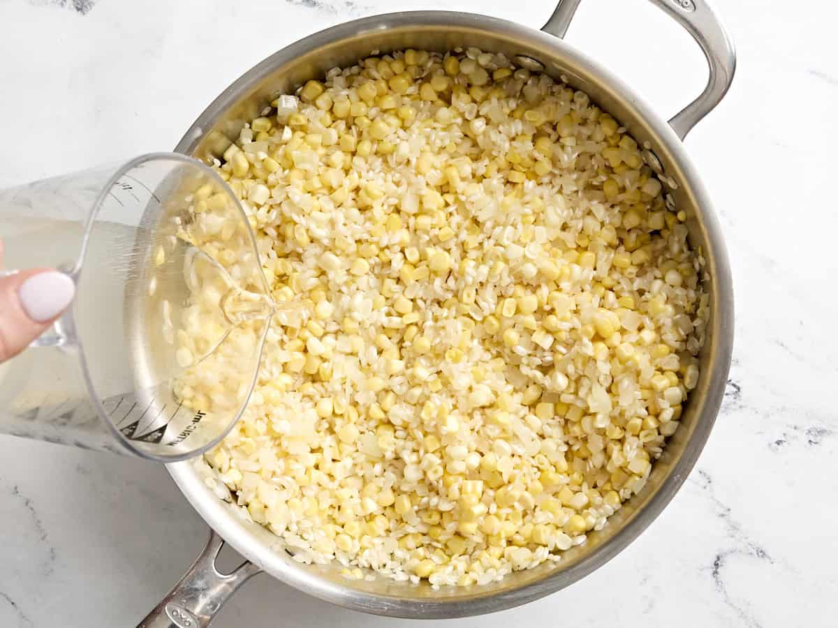White wine being poured into arborio rice and corn kernels in a skillet.