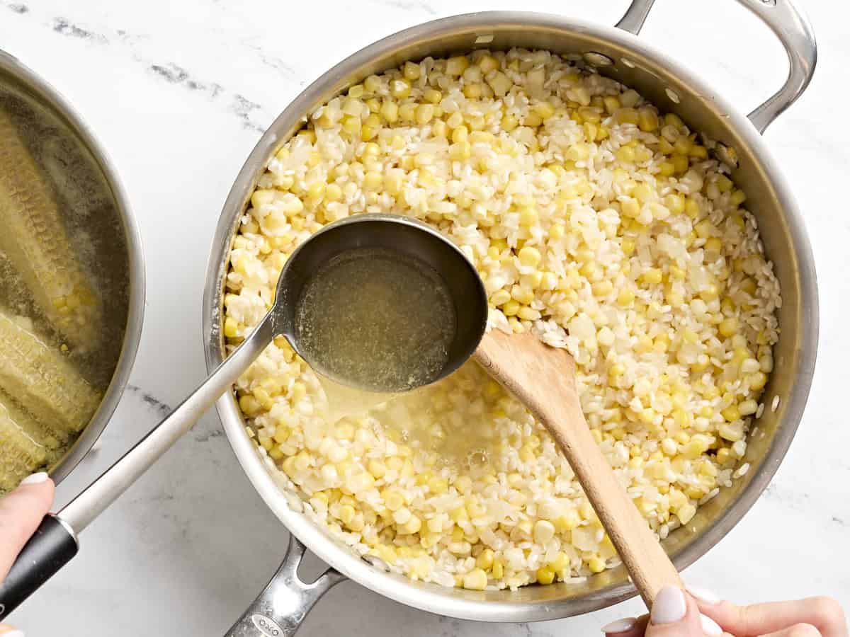 A ladle adding vegetable broth to sweet corn risotto in a skillet.