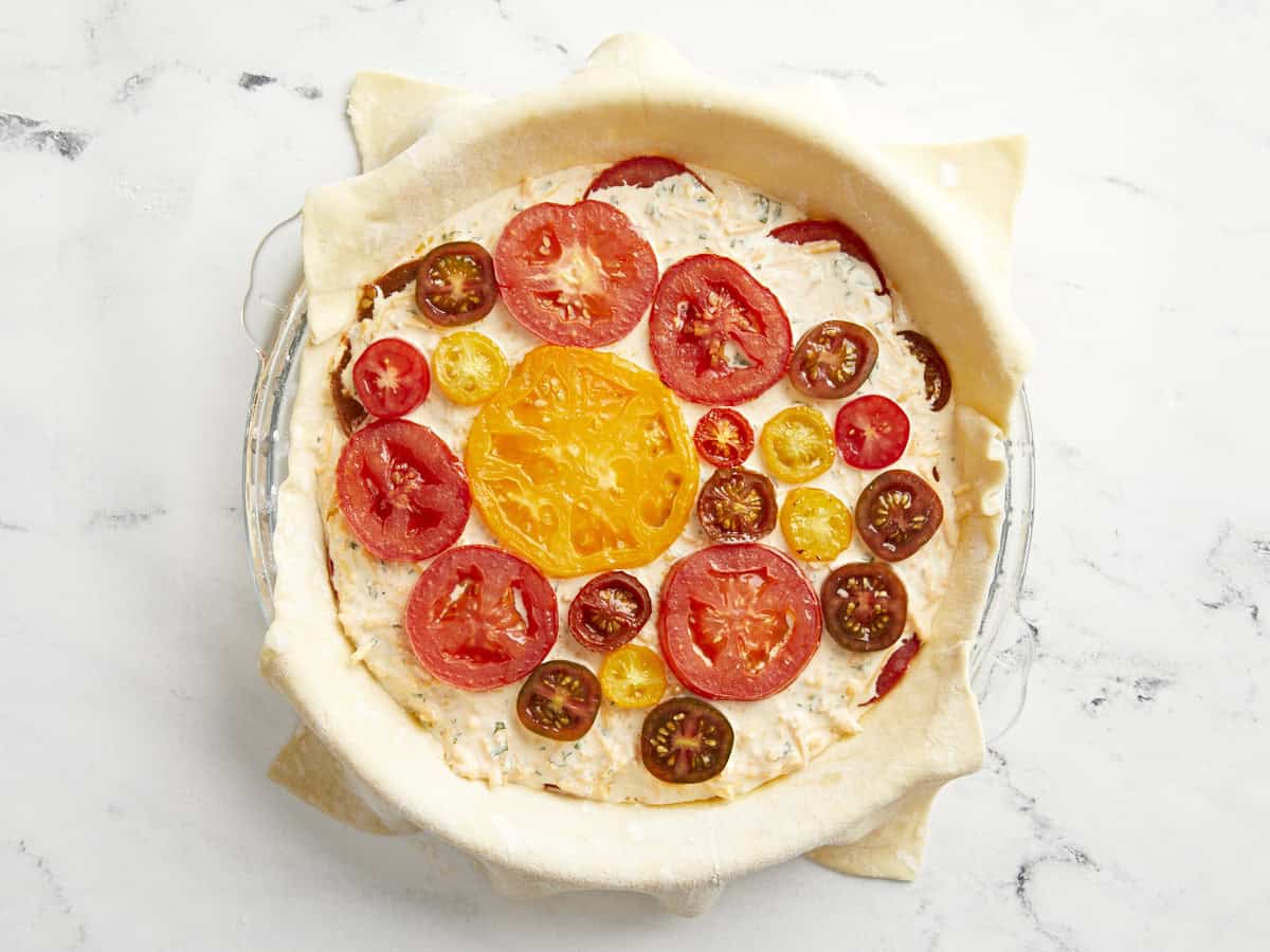 Puff pastry sheet in a glass pie pan filled with tomato pie filling