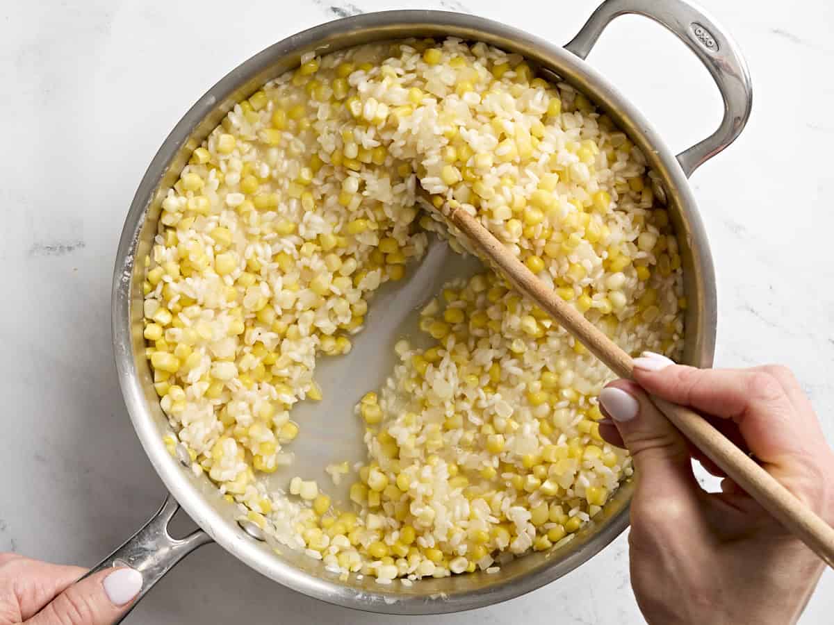 A wooden spoon stirring sweet corn risotto in a skillet.