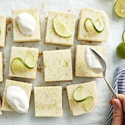 Key lime pie bars topped with whipped cream and lime slices.