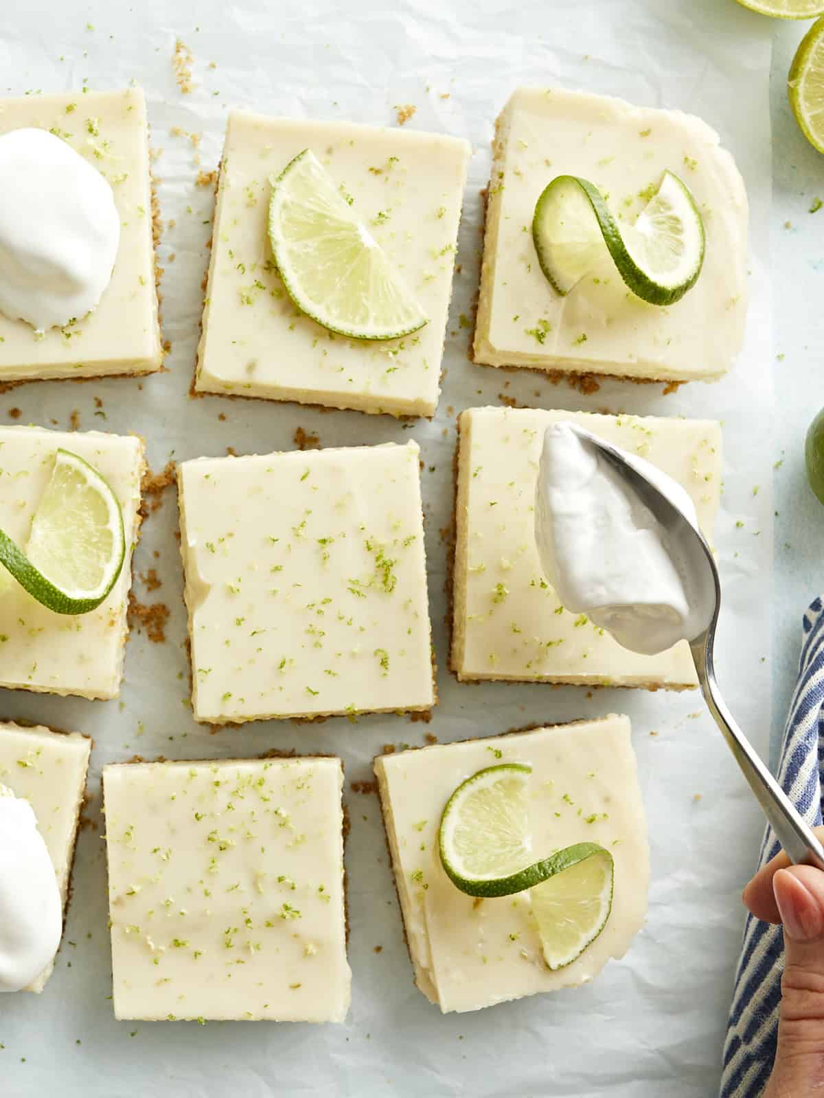 Key lime pie bars topped with whipped cream and lime slices.