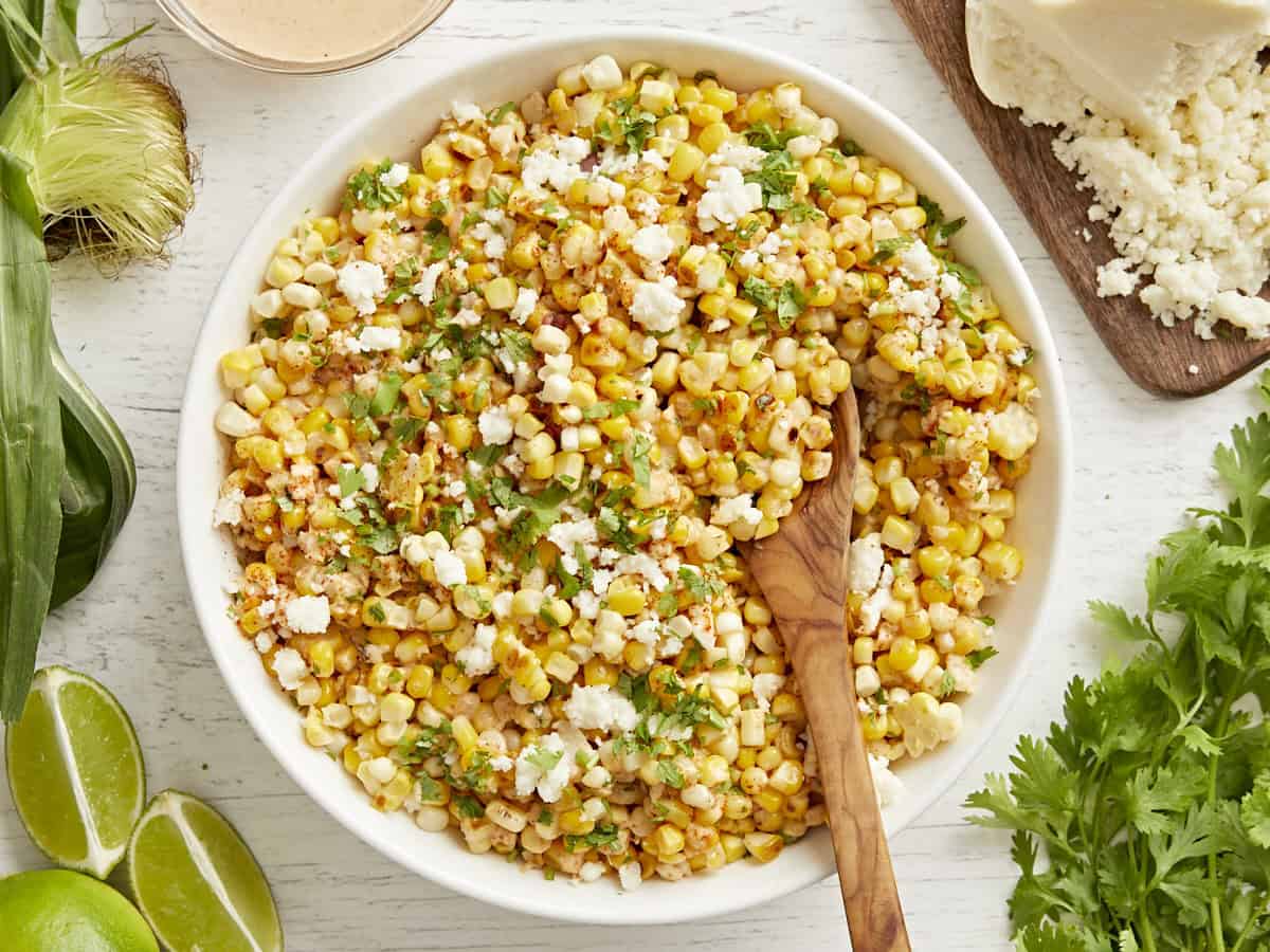 A wooden spoon in a bowl of Mexican street corn salad.