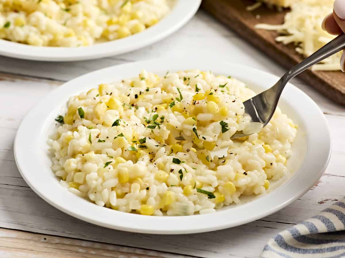 A fork scooping some sweet corn risotto off a plate.