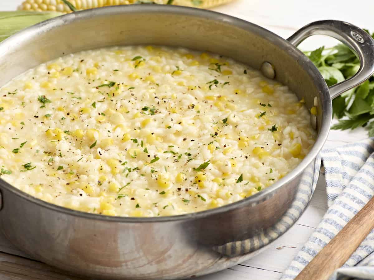 Sweet corn risotto in a skillet topped with fresh herbs.