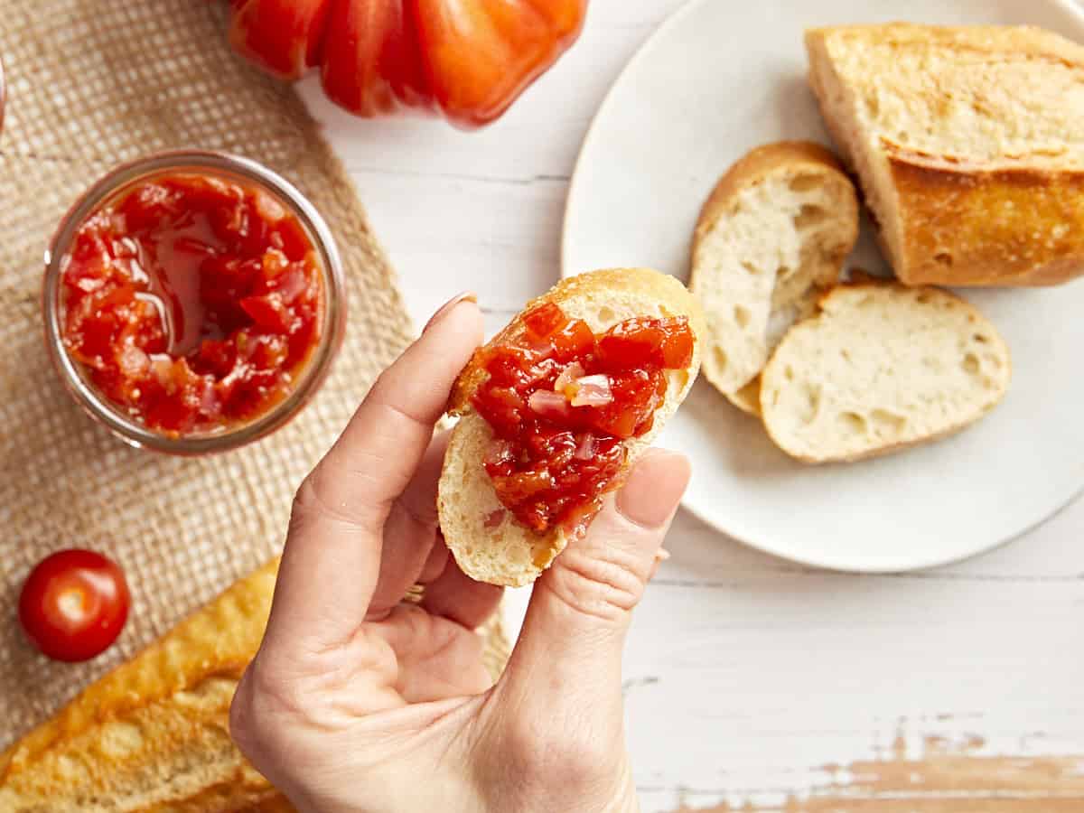 A hand holding a slice of bread topped with tomato relish.