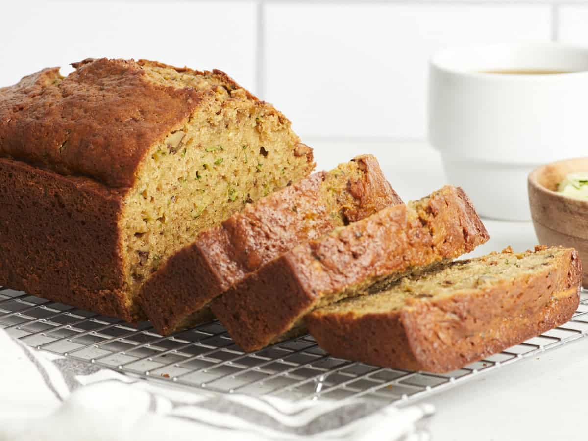 Side view of zucchini bread on a cooling rack with a cup of coffee on the side.