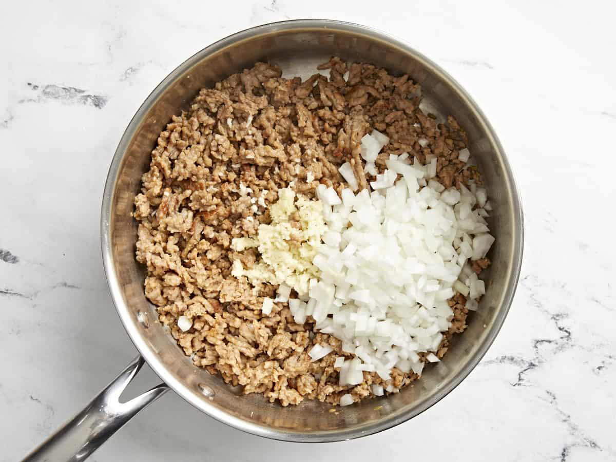 Onion and garlic added to sausage in a skillet.