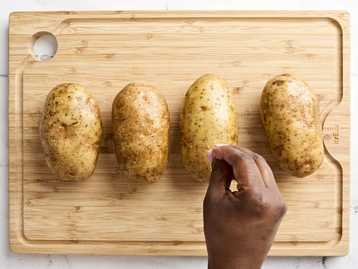 Four russet potatoes being brushed with oil and salted.