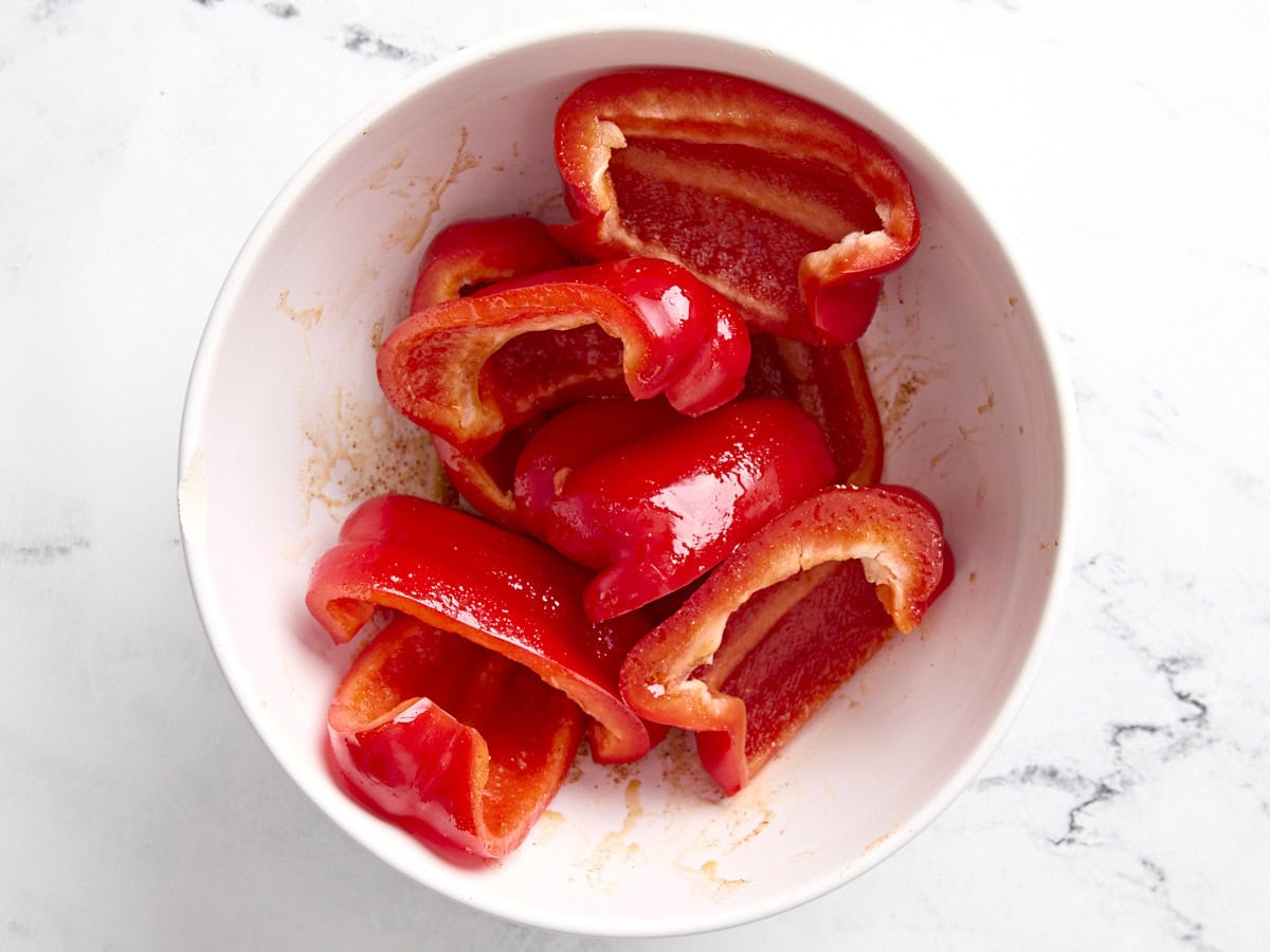 Quartered bell peppers being tossed in a seasoning mix for cauliflower tacos with romesco sauce