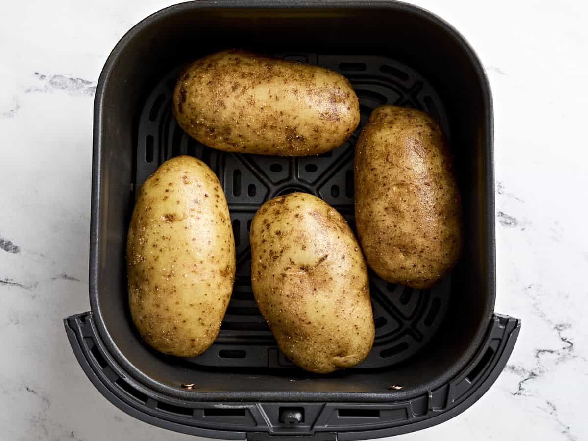 Four russet potatoes in an air fryer basket.