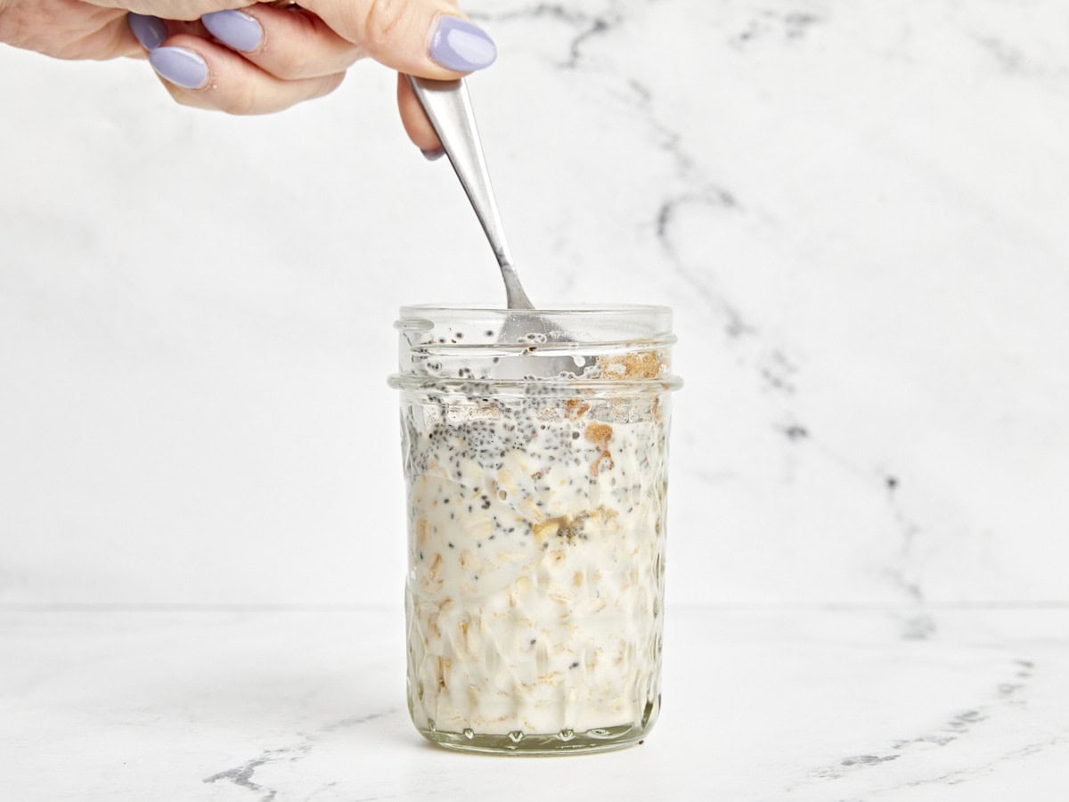 A spoon mixing the ingredients for overnight oats in a mason jar