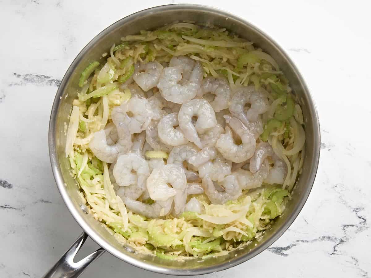 Raw shrimp added to a skillet with white mirepoix for shrimp and white beans