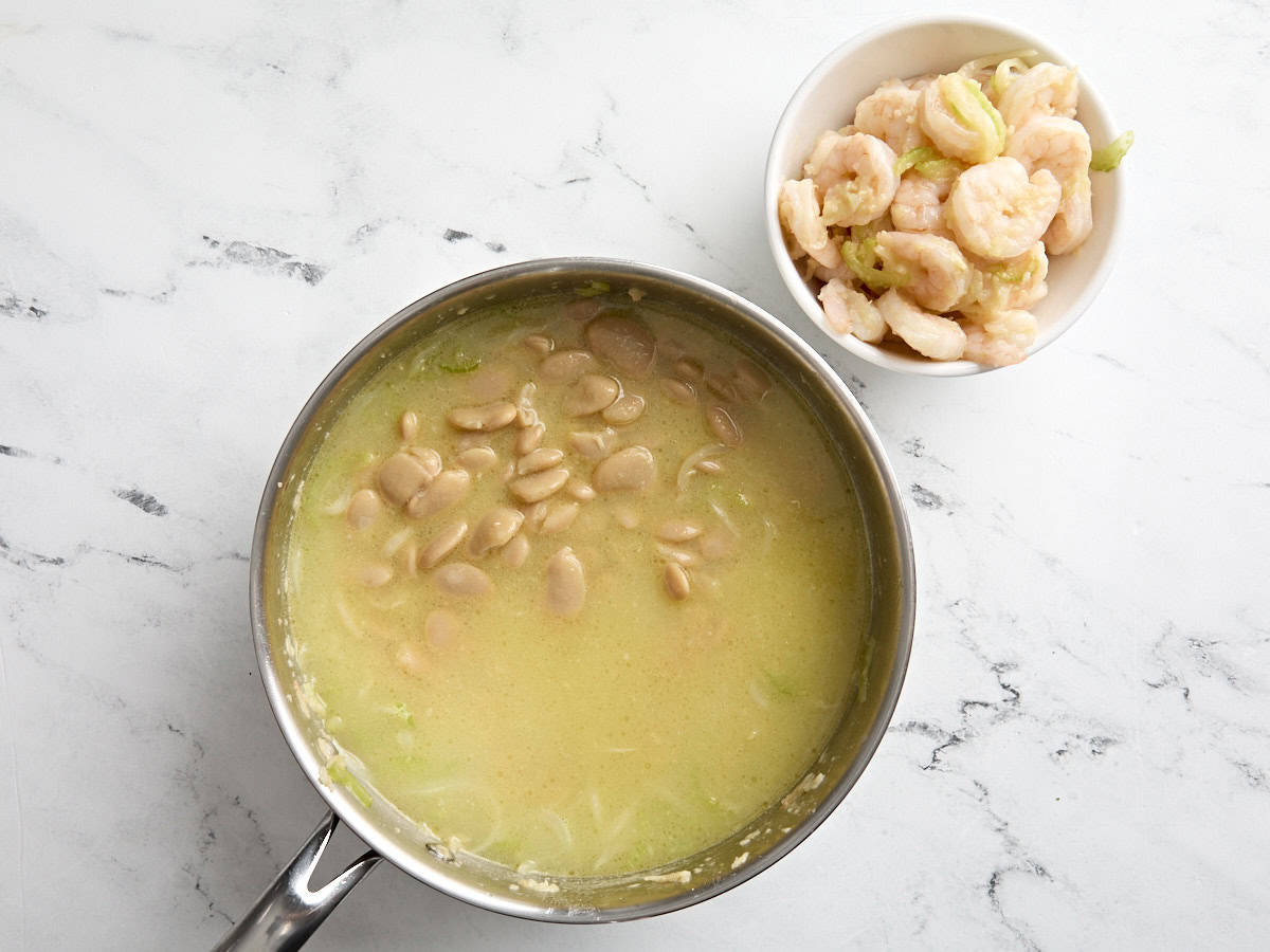 A skillet with chicken broth and white beans, next to a bowl of cooked shrimp