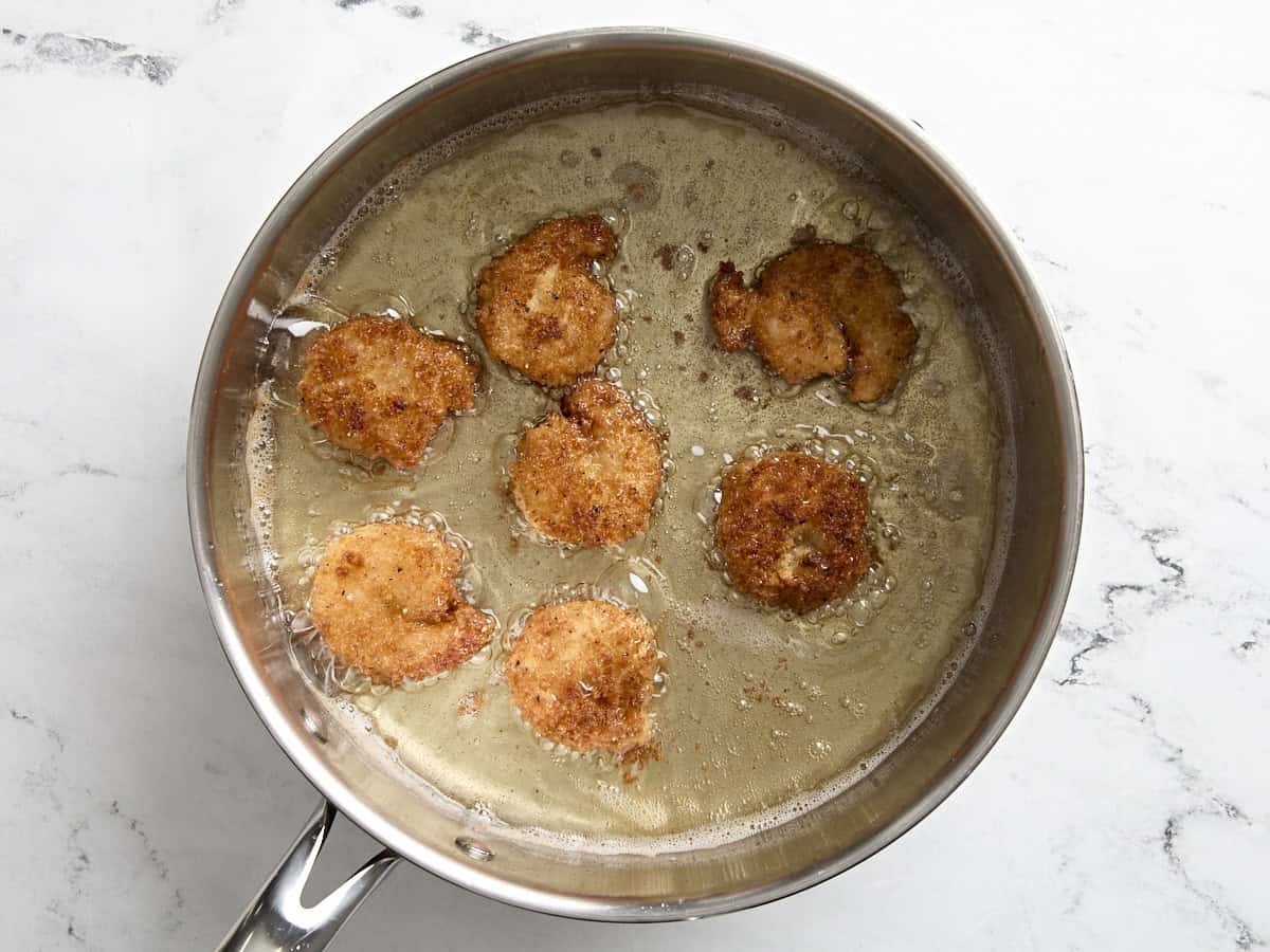 Golden brown breaded shrimp deep frying in a skillet