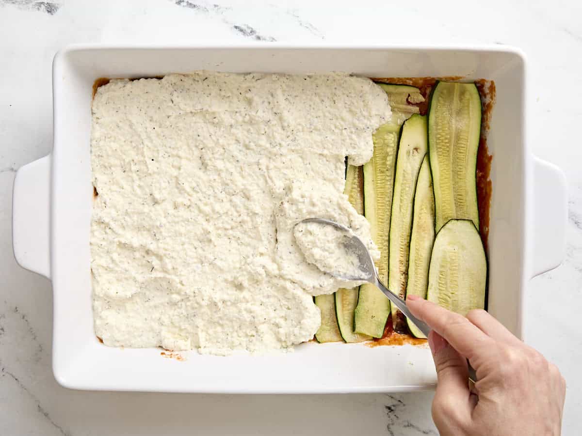 Sauce sauce being added to a zucchini lasagna in a baking dish