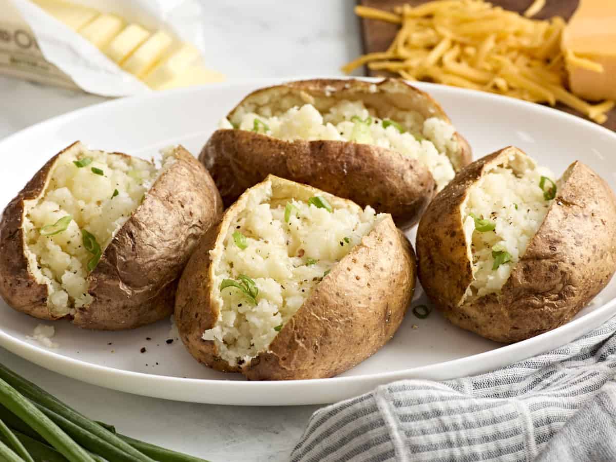 Side view of air fryer baked potatoes on a white platter.