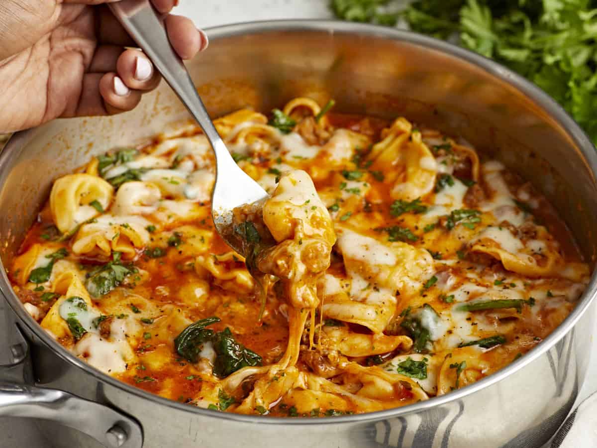 Side close up view of cheese tortellini and sausage skillet with a fork lifting some out.