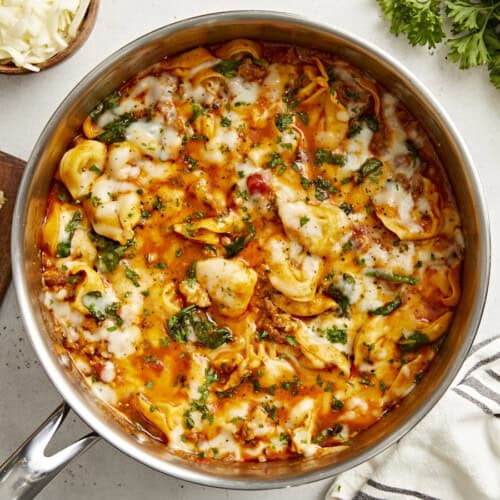 Overhead view of cheese tortellini and sausage skillet with garlic bread and parsley on the side.