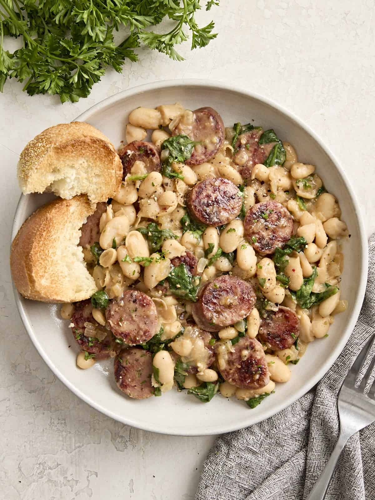 Overhead view of chicken sausage and white beans on a serving dish with toasted bread on the side.