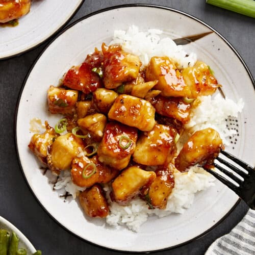 Overhead view of honey garlic chicken on a plate with white rice and a black fork.