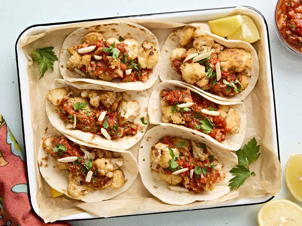 Overhead view of cauliflower tacos with romesco sauce in a parchment lined baking dish