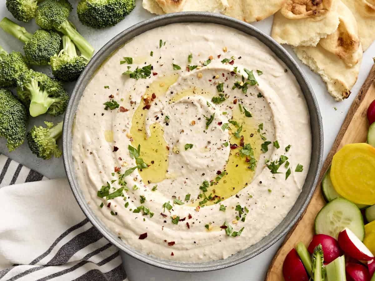 A bowl of white bean hummus topped with olive oil and fresh herbs