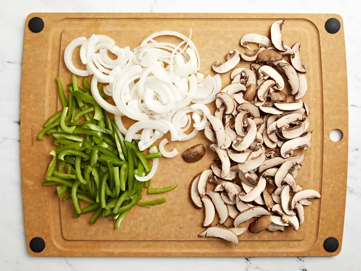 Peppers, onion and sliced mushrooms on a cutting board.