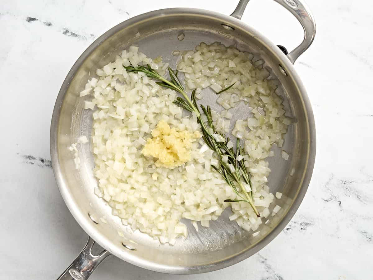 Minced garlic added to diced onion and rosemary in a skillet.