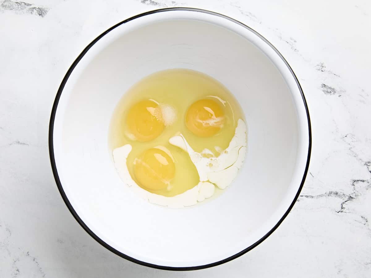 Cracked eggs and half and half in a mixing bowl.