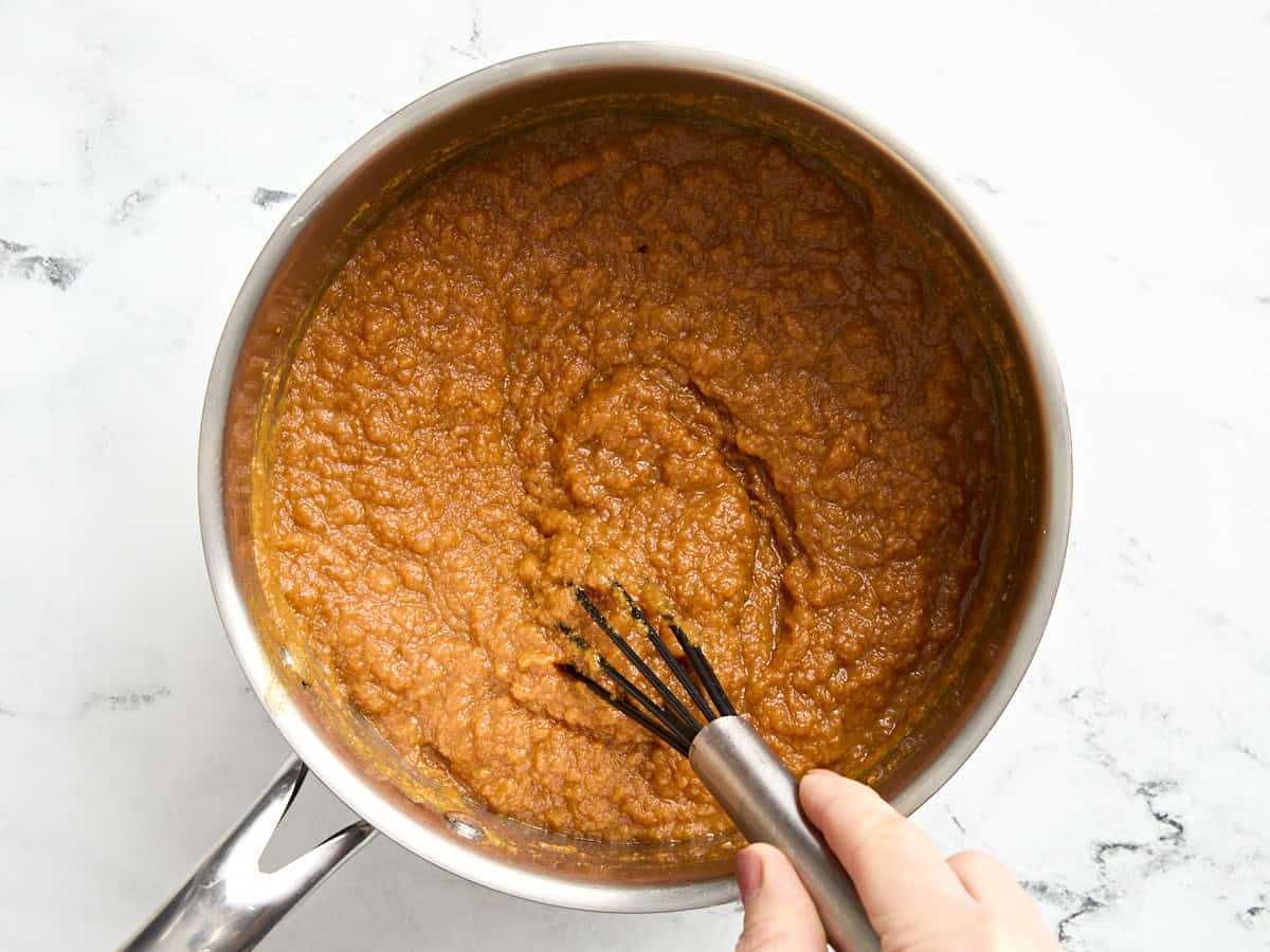 A whisk mixing the ingredients for pumpkin butter in a saucepan.