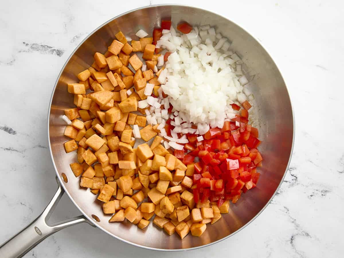 Onion and bell pepper added to sweet potatoes in a skillet.