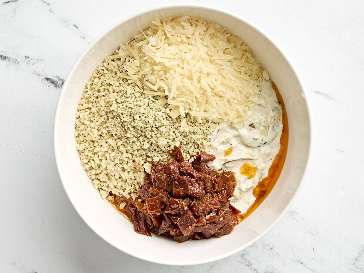 Stuffed mushroom filling with parmesan, sun dried tomatoes and breadcrumbs in a mixing bowl.