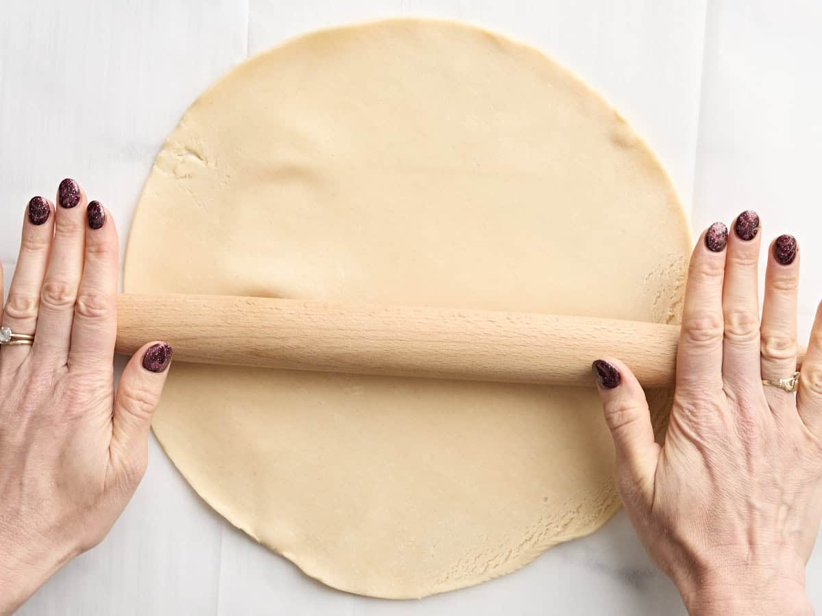 Hands using a rolling pin to roll out premade pie crust.