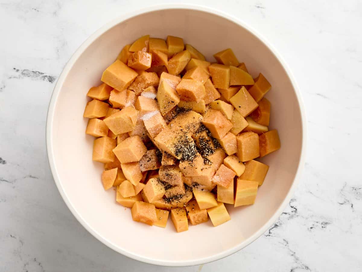 Butternut squash cubes in a baking bowl with garlic powder, salt, and black pepper.