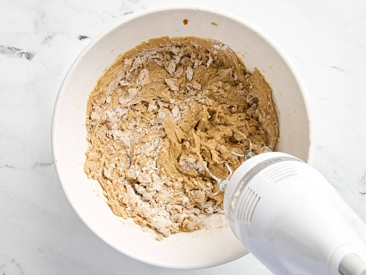 Pumpkin cookie dough in a mixing bowl with a hand mixer.